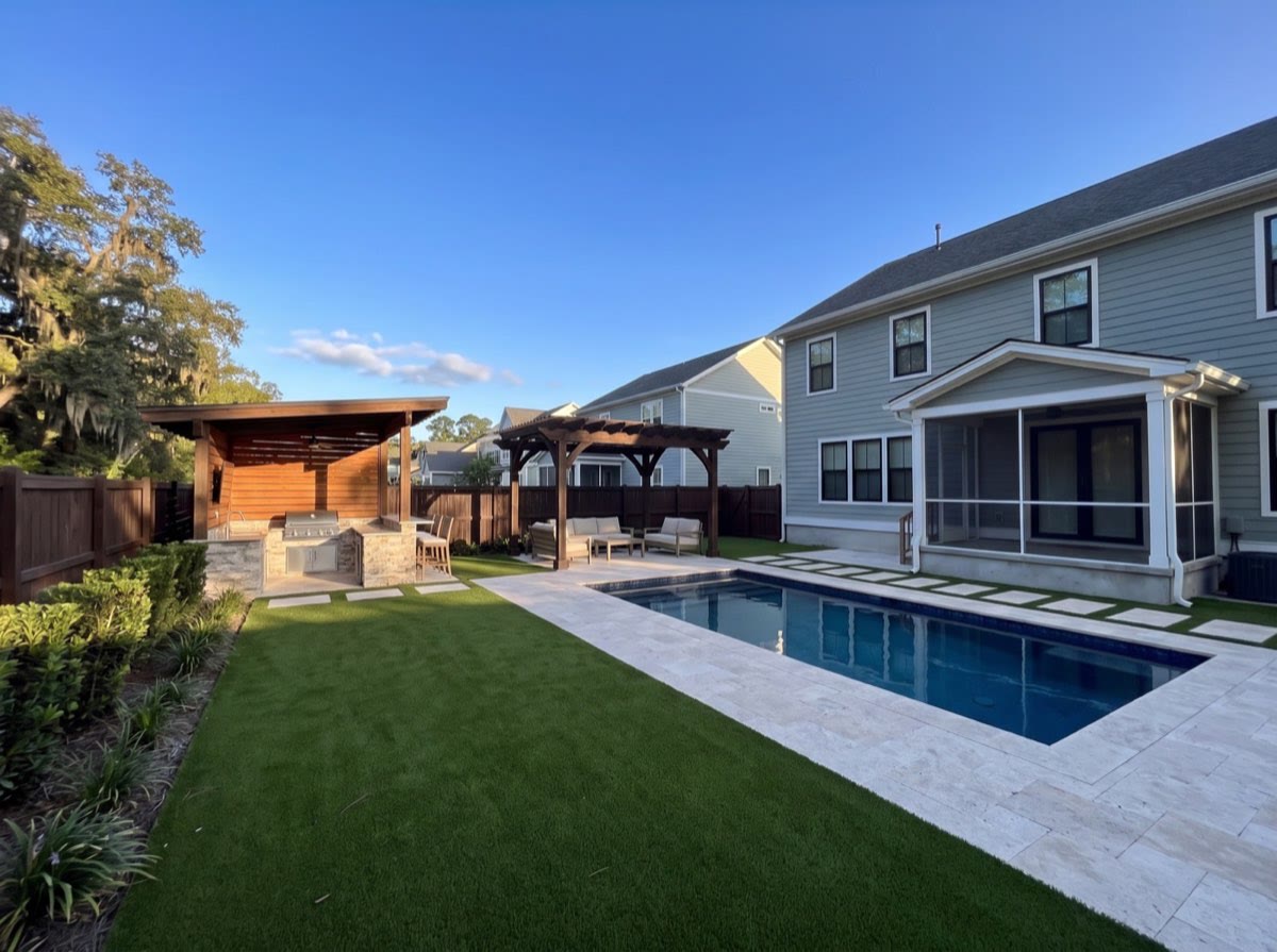 The same garden laid with artificial turf and travertine, with a pool, kitchen and pergola